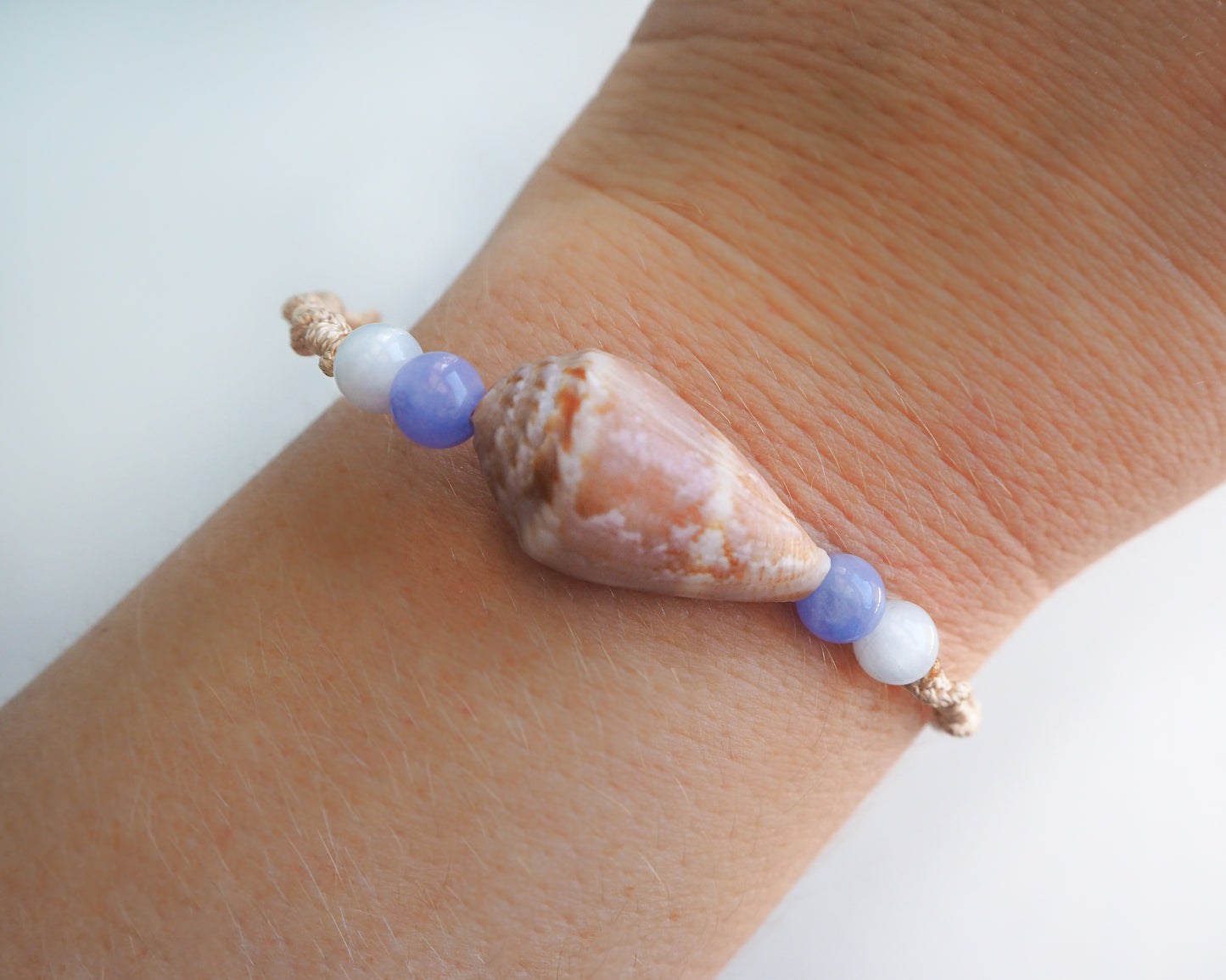 Close up of wrist model with Angelite Cone Shell Bracelet and white background. Handmade bracelet with handpicked cone shell from Portugal and gemstone beads on display.