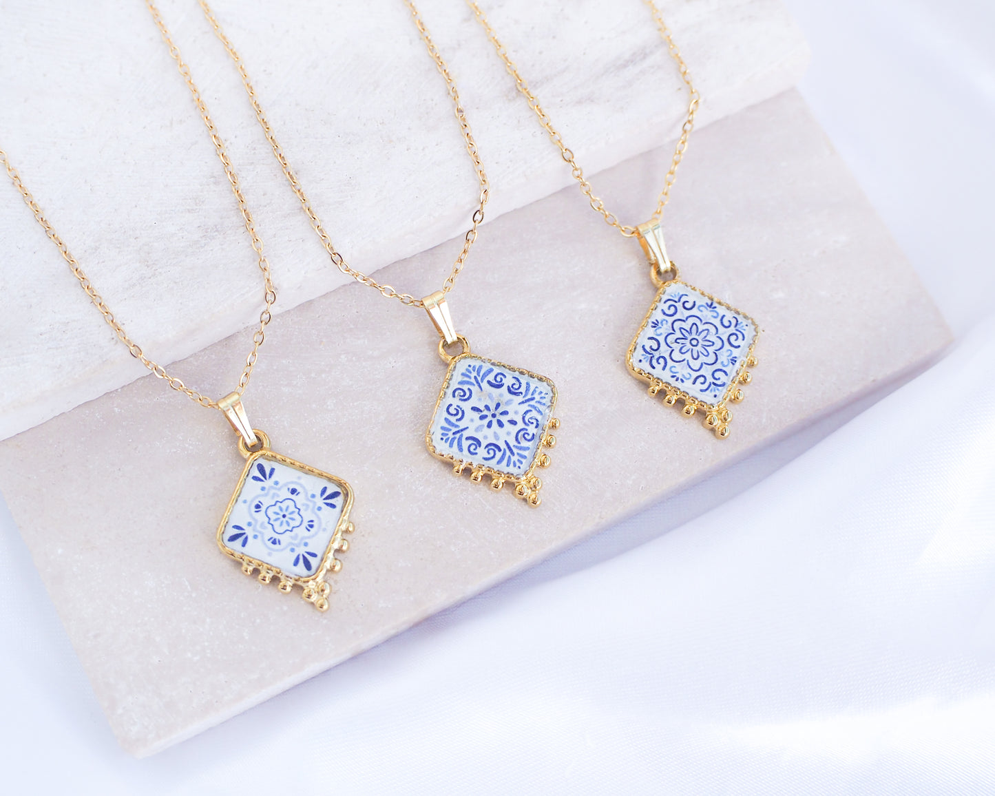 Portuguese Tile Necklaces Floral Blue Gold on stone displayed. Made with 18k gold stainless steel and white blue floral pendant inspired by the Portuguese Azulejo design pattern.