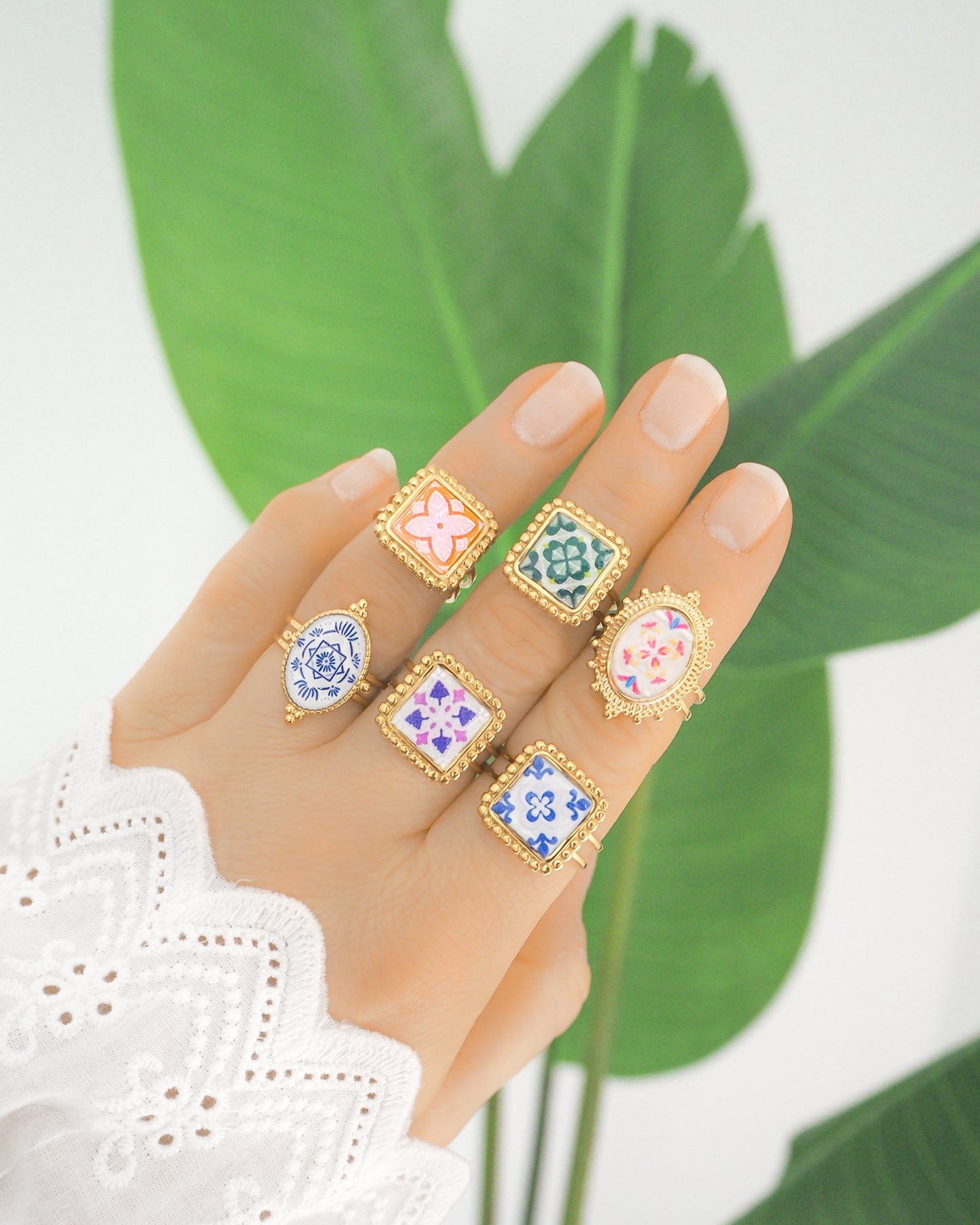 Hand wearing Gold Portuguese Tile Rings with green plant background. Rings are handmade with 18k gold stainless steel and are made with different patterns inspired by the Portuguese azulejos tiles.