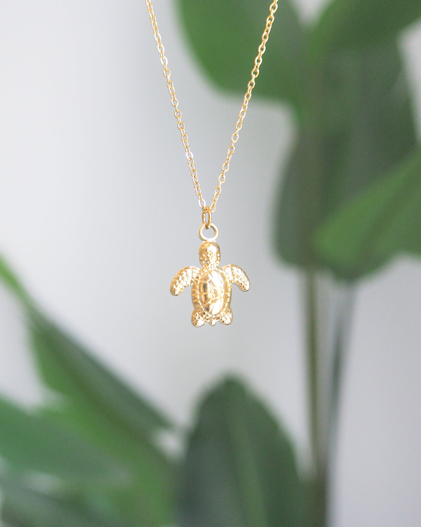 Gold turtle pendant necklace with a green leafy background