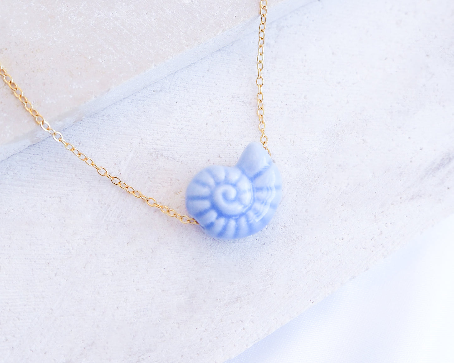 Blue Ceramic Seashell Nautilus Gold Necklace displayed on stone