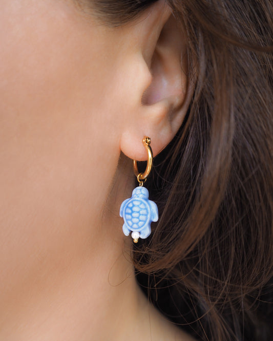 Close-up of an ear wearing a gold hoop earring with a blue turtle charm.