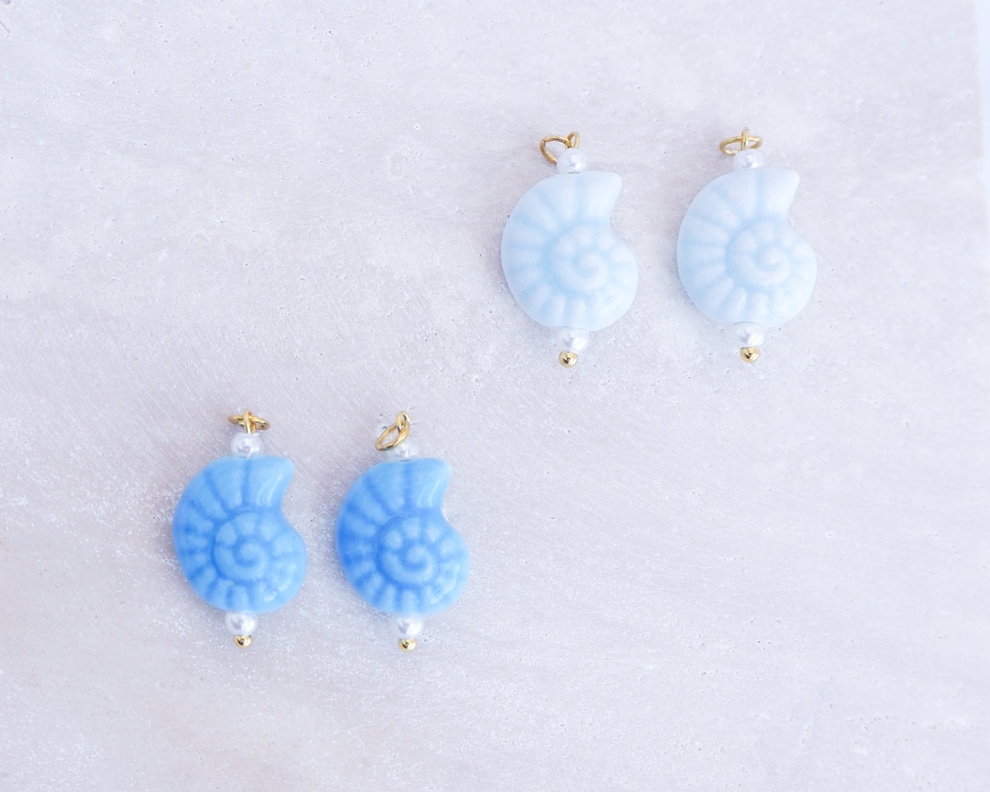 Pair of blue ceramic seashell charm earrings on a light gray background
