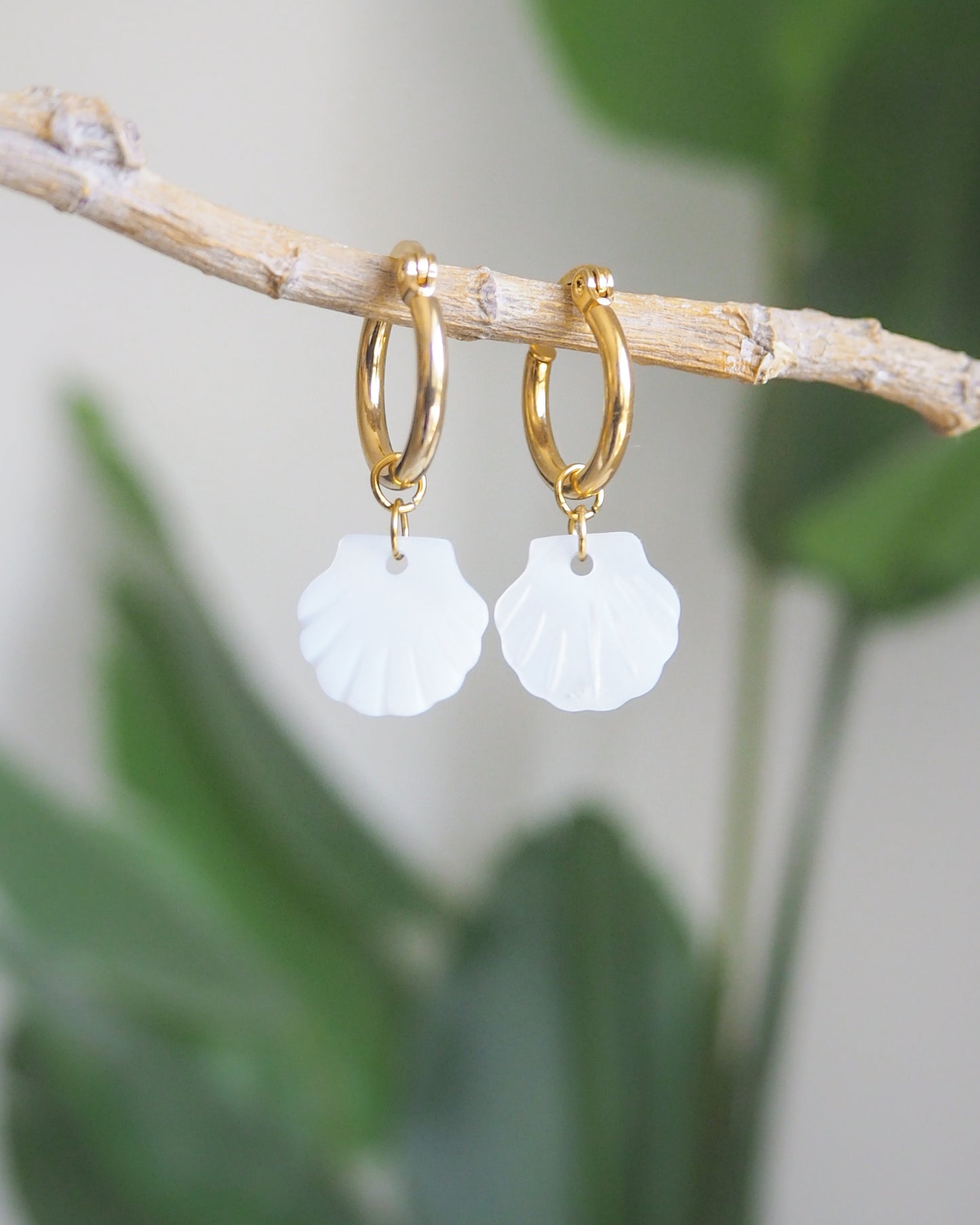 Close-up of gold hoop earrings with mother-of-pearl shell pendants