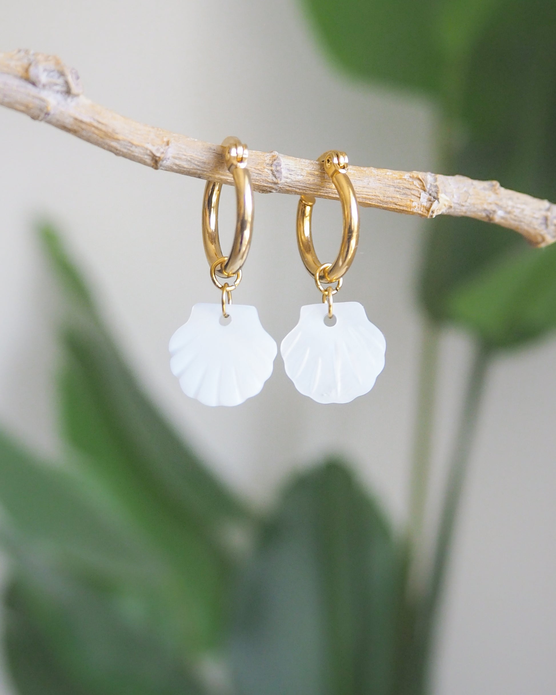 Close-up of gold hoop earrings with mother-of-pearl shell pendants