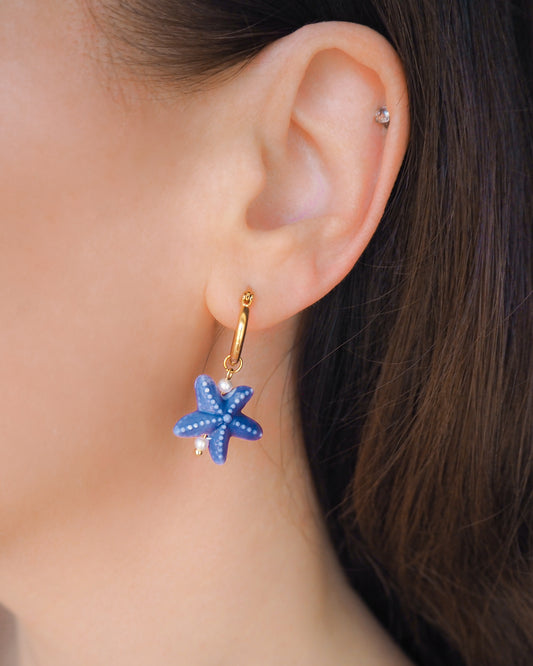 Dark Blue Ceramic Sea Star Gold Hoop Earrings in ear model, 14k gold stainless steel earring hoops with blue ceramic starfish pendants, ocean inspired jewelry from Portugal