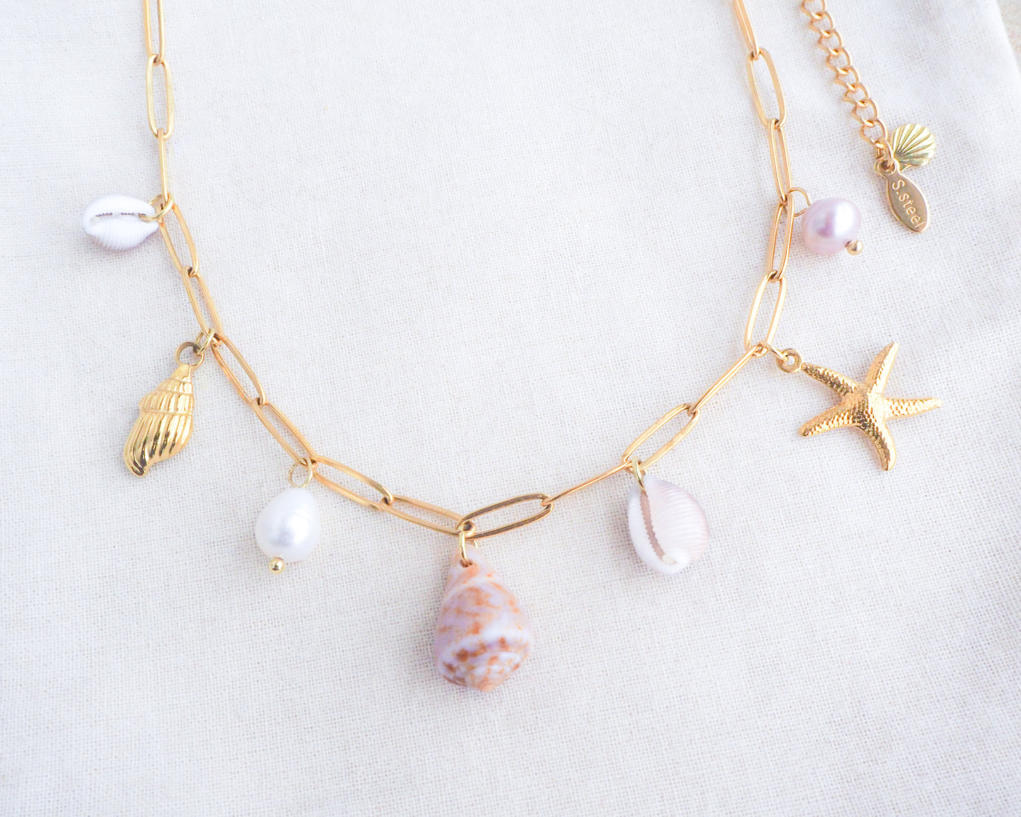 Gold Ocean Shell Charm Necklace on display front view, with tiny cone and cowrie shells, freshwater pearls, starfish sea star and whale tail pendants.