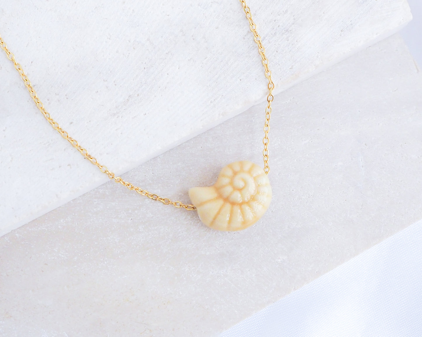 Gold Bege Ceramic Seashell Nautilus Necklace displayed on stone