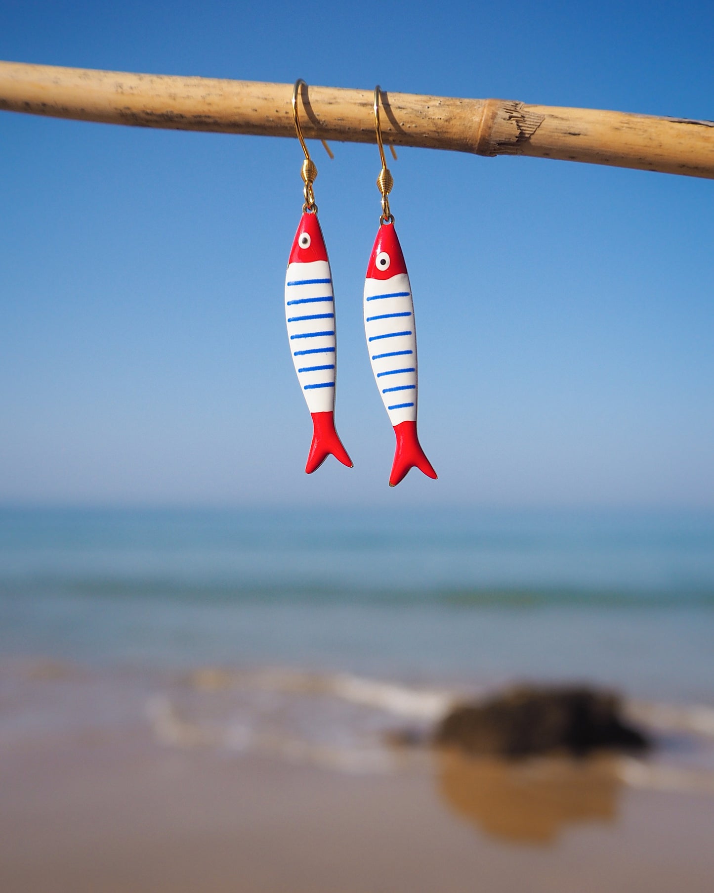 Close up of Nautical Striped Sardine Fish Earrings with ocean background, Red Blue White Striped Fish Pendant, Beautiful gift for Portugal lovers or holiday memory, coastal jewelry from Portugal