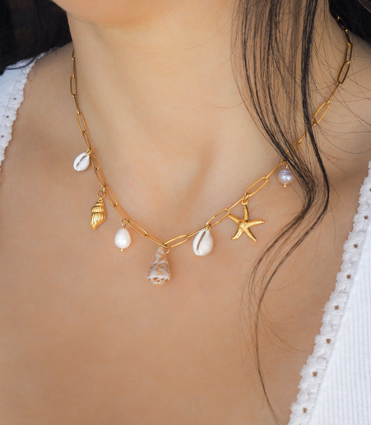 Gold Ocean Shell Charm Necklace on neck model, with tiny cone and cowrie shells, freshwater pearls, starfish sea star and whale tail pendants.