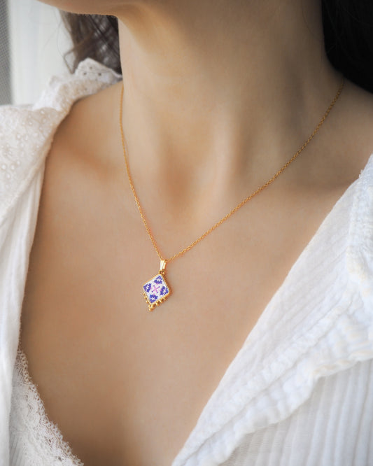 Model wearing Purple Pink Portuguese Tile Necklace Gold on stone displayed. Made with 18k gold stainless steel and white purple pink pendant inspired by the Portuguese Azulejo design pattern.