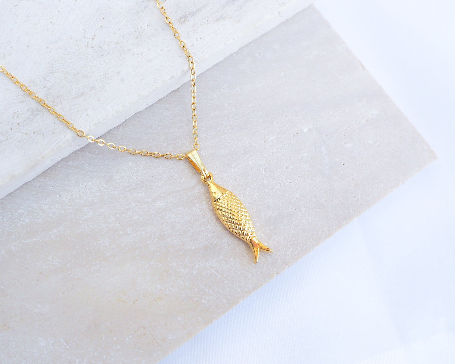Gold Sardine Fish pendant necklace on a marble surface