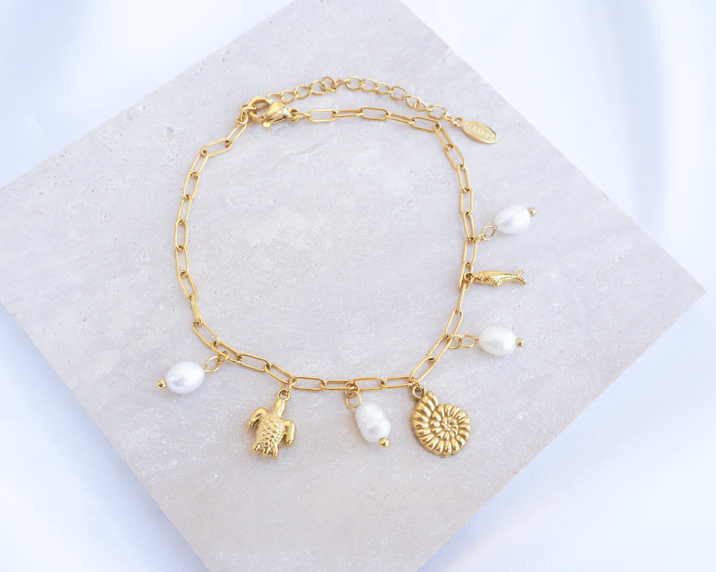 Gold charm bracelet with freshwater pearls and ocean charms on display, tiny turtle pendant, tiny nautilus pendant, tiny sardine fish pendant bracelet.