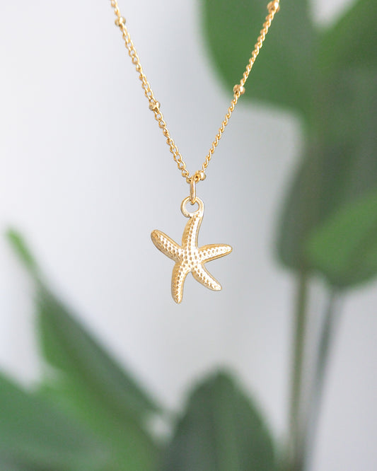 Gold starfish pendant necklace on a blurred green leaf background