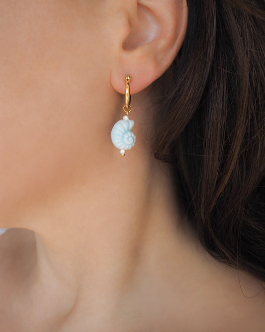 Close-up of an Ceramic Seashell Light Blue Gold Earring Hoops worn by a person with a blurred background