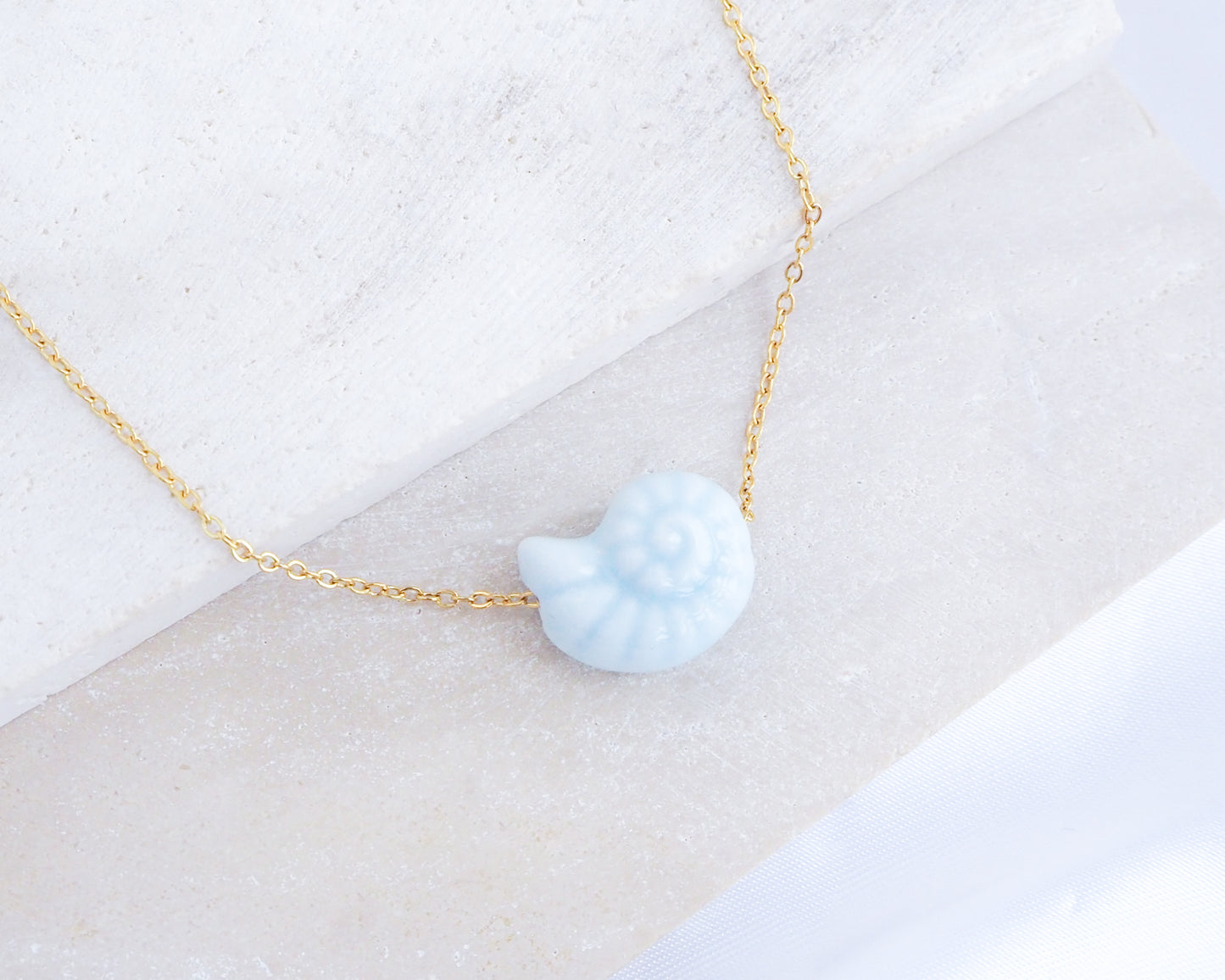 Light Blue Ceramic Seashell Nautilus Gold Necklace displayed on stone