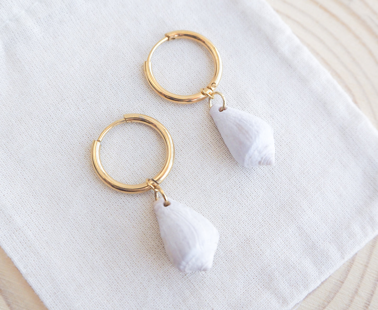 Close up of Light Mediterranean Cone Shell Gold Earring Hoops on displayed, handpicked cone shells from Portugal, 18k gold stainless steel shell earring hoops, seabylou