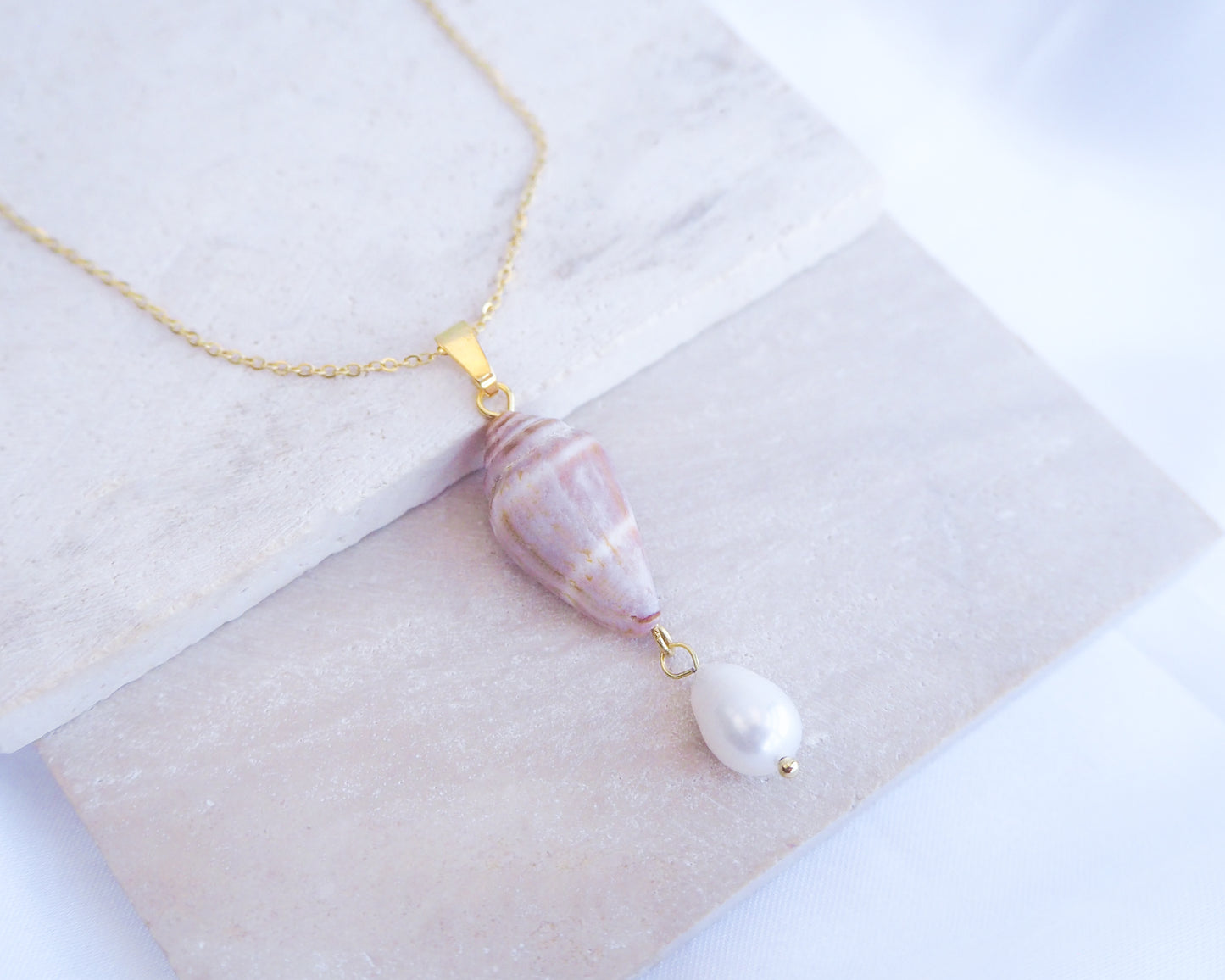 Close up of Model wearing Mediterranean Cone Shell Pearl Necklace Reversed from Portugal on stone, handpicked cone shell from Algarve, Freshwater pearl and 18k gold stainless steel chain