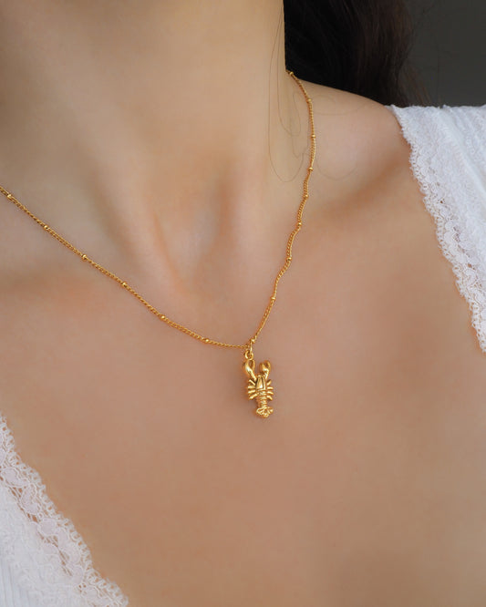 Model wearing Gold Lobster Necklace on stone displayed, made with 18k gold stainless steel, coastal jewelry from Portugal
