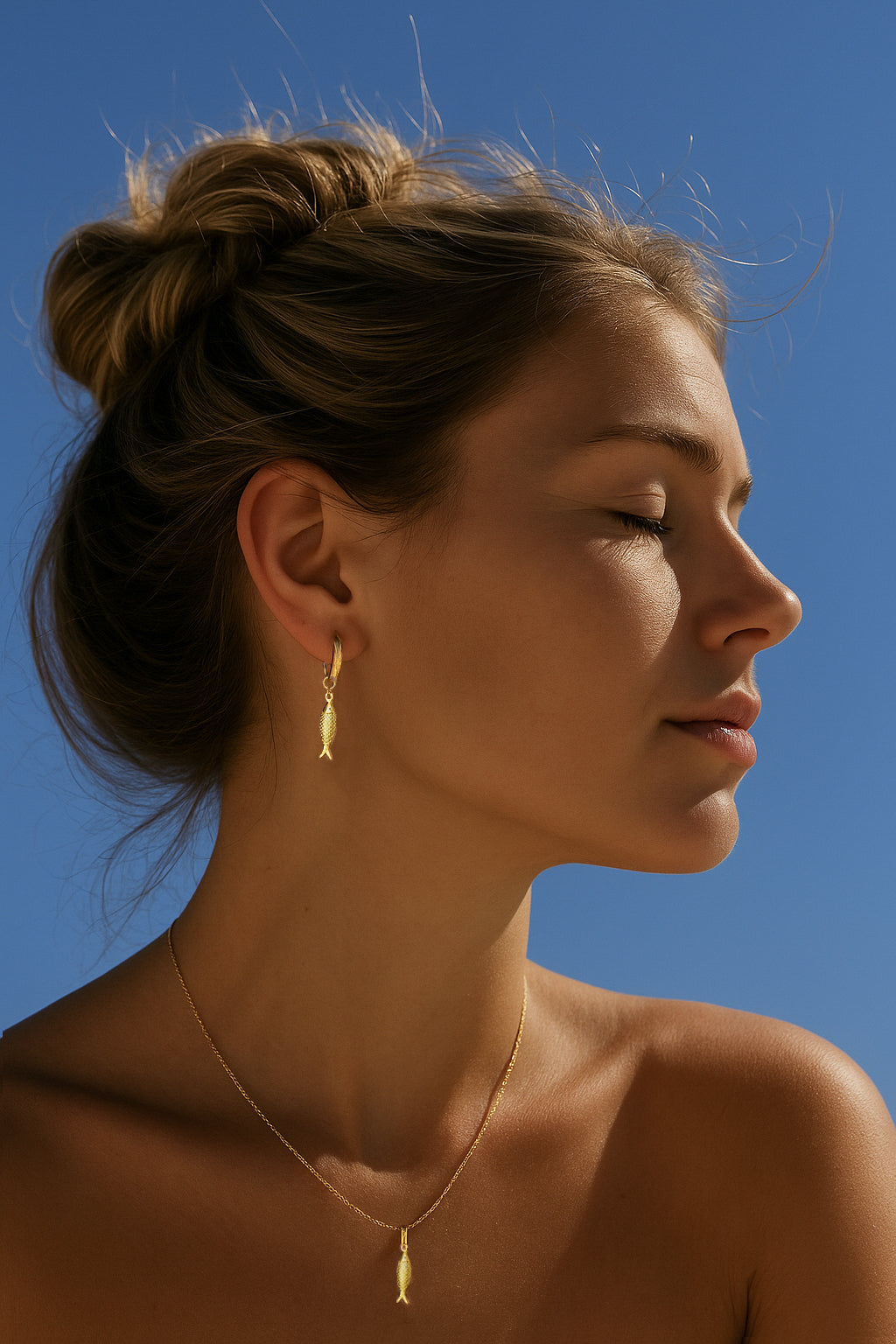 Model with bun in the sun wearing Gold Sardine Fish Earrings in ear of model and sardine fish necklace on neck of model.