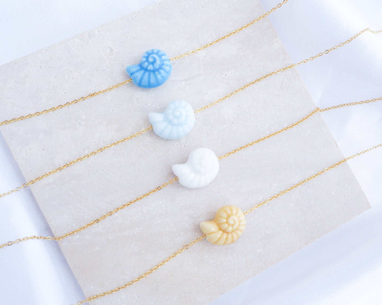 Ocean Blue Ceramic Seashell Nautilus Gold Necklaces displayed on stone