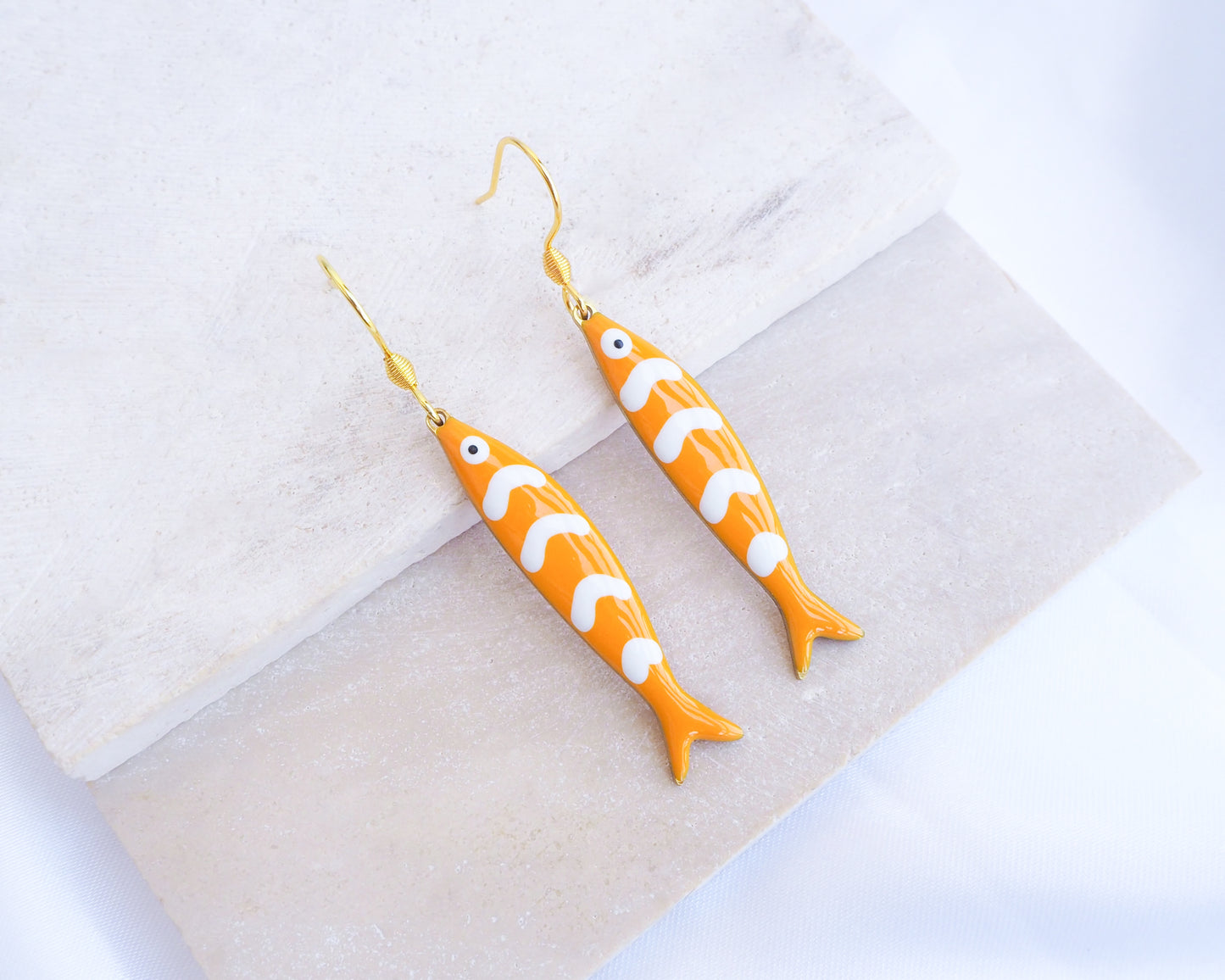 Orange Sardine Fish Earrings with 14k gold stainless steel earring hooks displayed on stone, Beautiful gift for Portugal lovers or holiday memory, coastal jewelry from Portugal