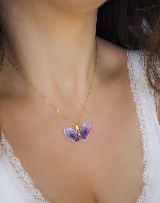 Purple butterfly pendant on a gold chain worn by a person