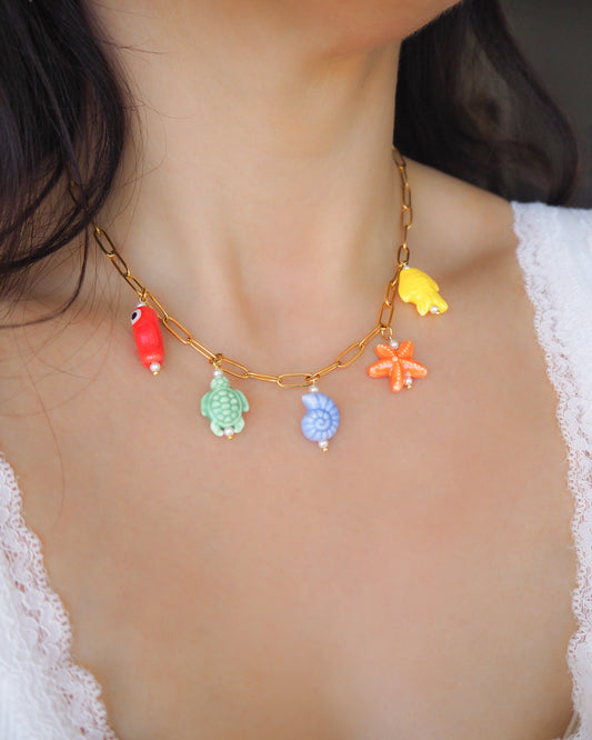 Model wearing Rainbow Ceramic Charm Necklace with 5 ceramic ocean charms (turtle, starfish, fish, shell & more), sea treasure pendants, 18k gold stainless steel chain