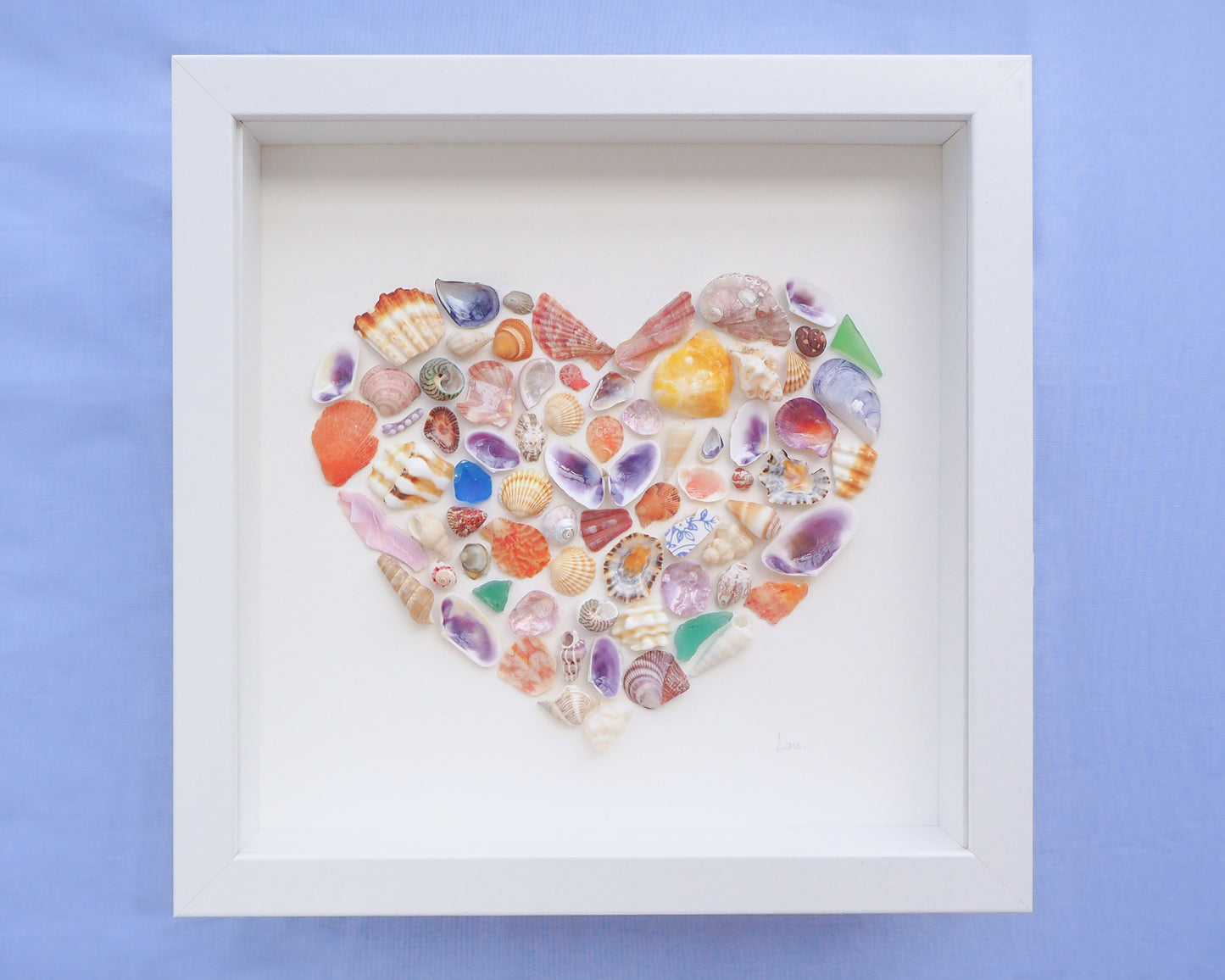 Heart-shaped arrangement of colorful seashells in a white frame on a blue background. Close up of Rainbow Seashell Heart Artwork with colorful shell handpicked from Portugal. Coastal Home Wall Decor, Shell Wall Art, Handmade Shell Artwork, Cute Coastal Nursery Decoration