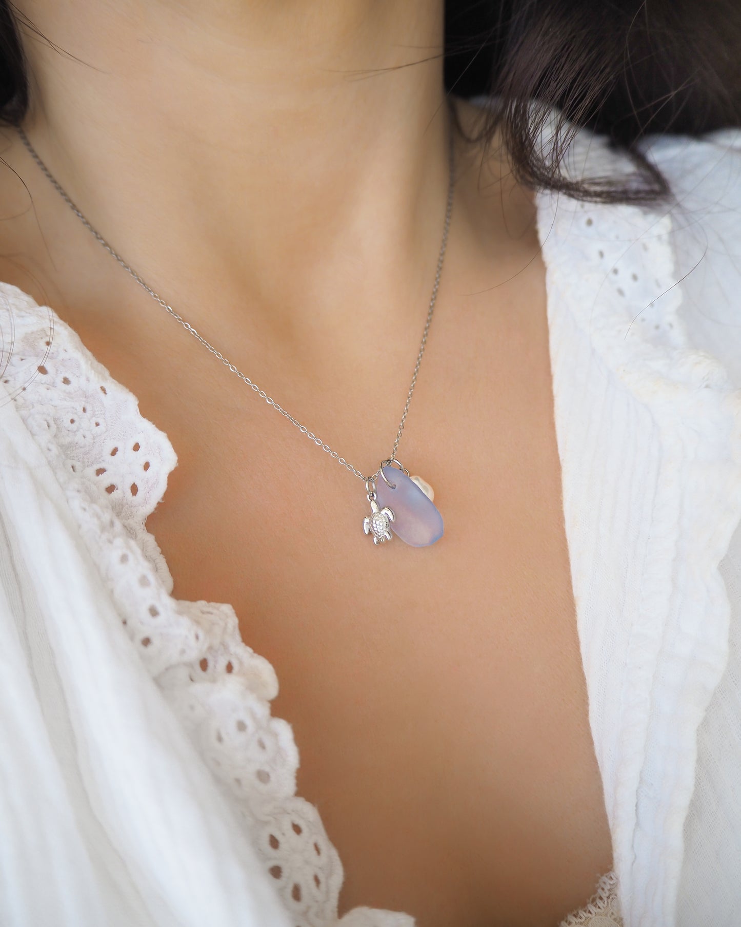 Model wearing a silver necklace with a tiny turtle pendant, light blue sea glass and freshwater pearl pendant on neck with white shirt. Made with silver stainless steel chain.