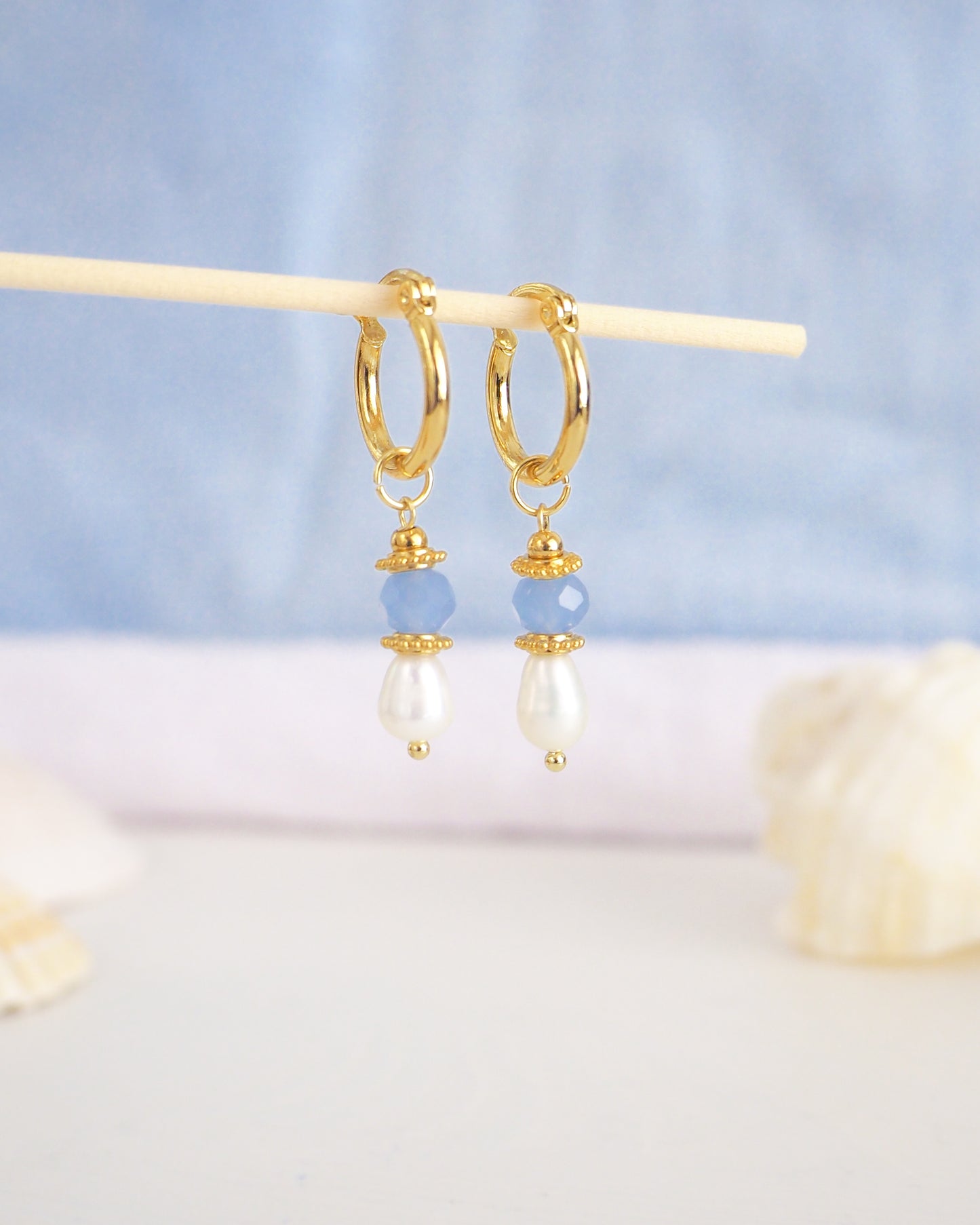 Gold hoop earrings with pearls and blue beads on a light blue background. Handmade with blue sparkling crystal beads, ivory freshwater pearls and 18k gold stainless steel beads. These earrings are inspired on the ocean is part of the ocean serenity pearl collection.
