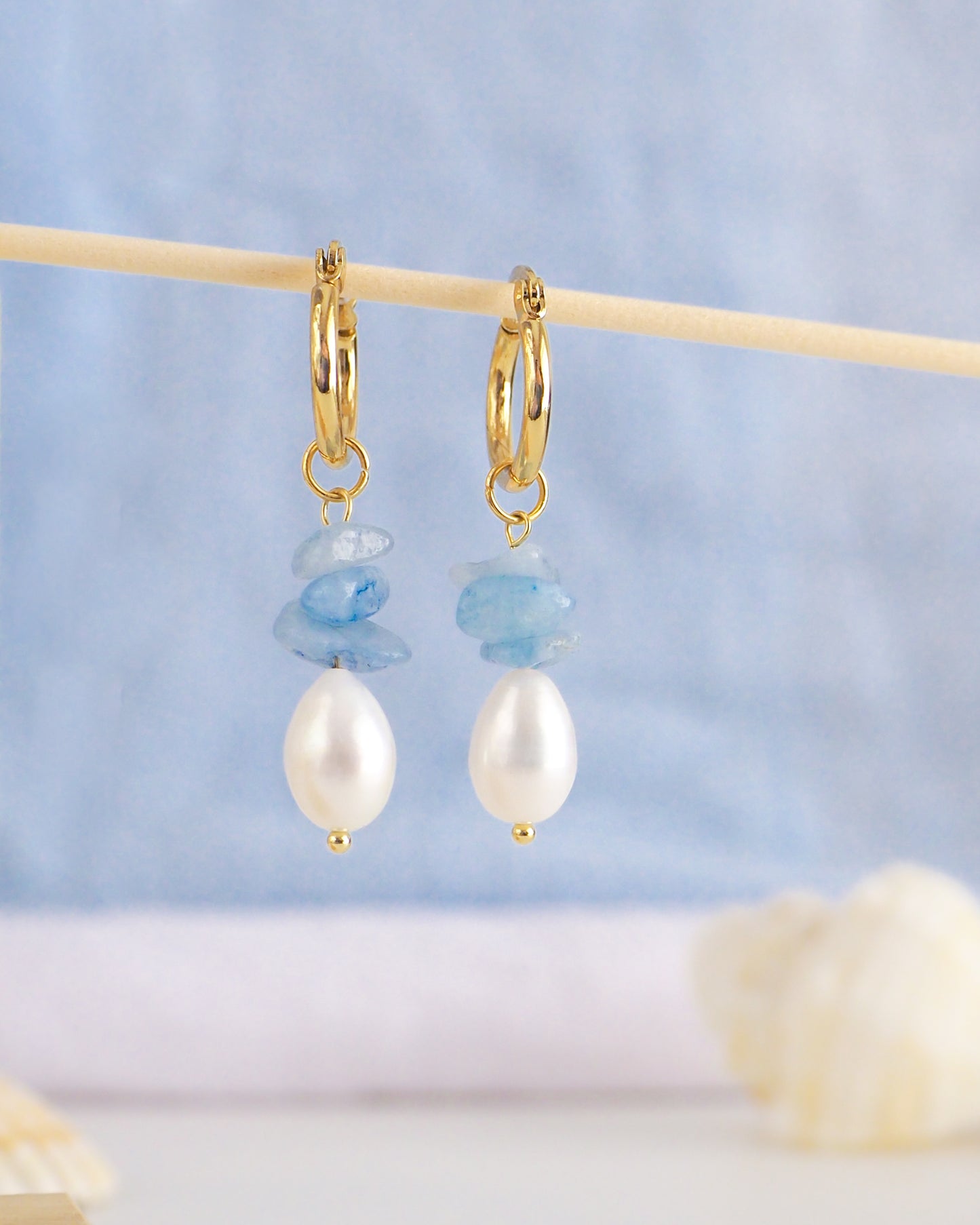 Front view of gold hoop earrings with light blue background. Made with 14k gold stainless steel, aquamarine gemstone beads and freshwater pearls.