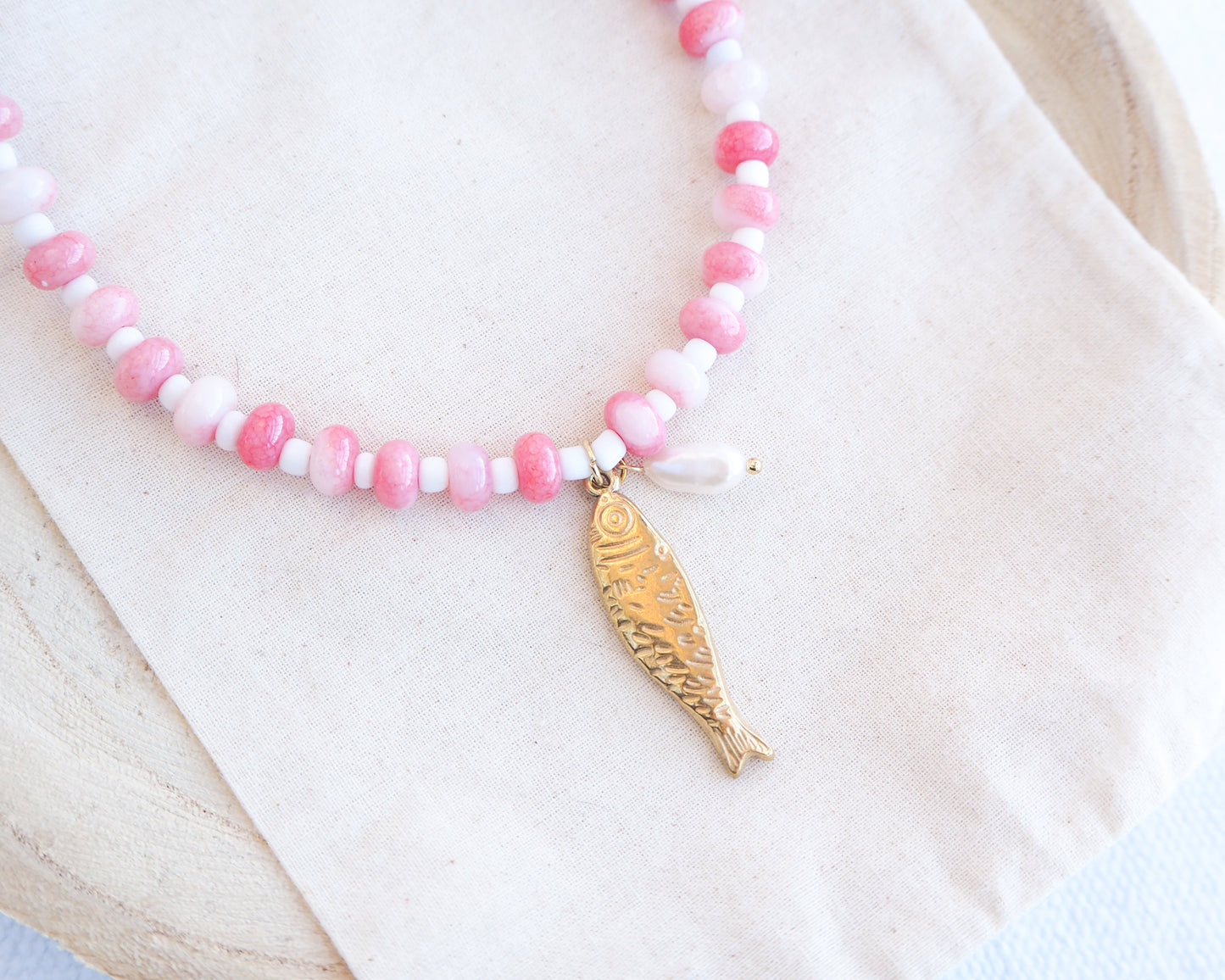 Necklace with pink and white beads and a gold sardine fish pendant and freshwater pearl bead on a person wearing a white top. The necklace is made with seed beads and freshwater pearls and a big gold sardine fish The sardine fish pendant is made of 18k gold stainless steel.