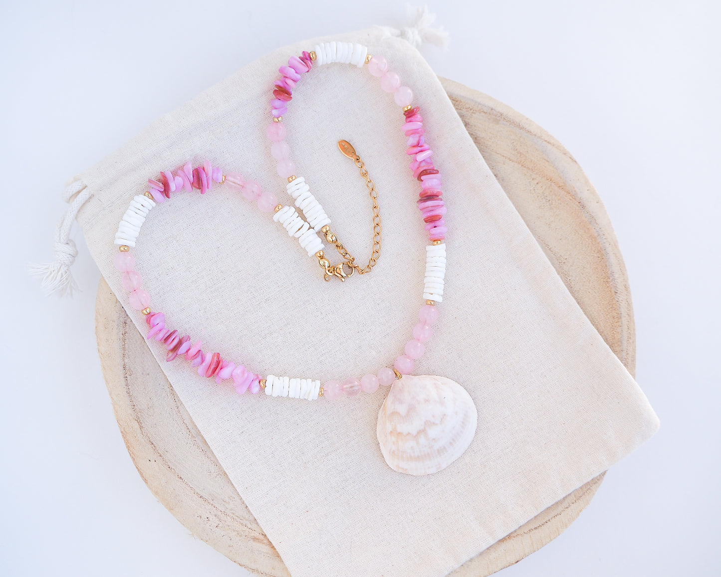 Front view big clam necklace with pink and white beads and a shell pendant on display. Shell is paired with rose quartz gemstone beads, soft pink stones and white shell beads. The shell is a Norwegian cockle shell handpicked from Portugal and is about 4 cm. The color of the shell is ivory white with a beige brown pattern.