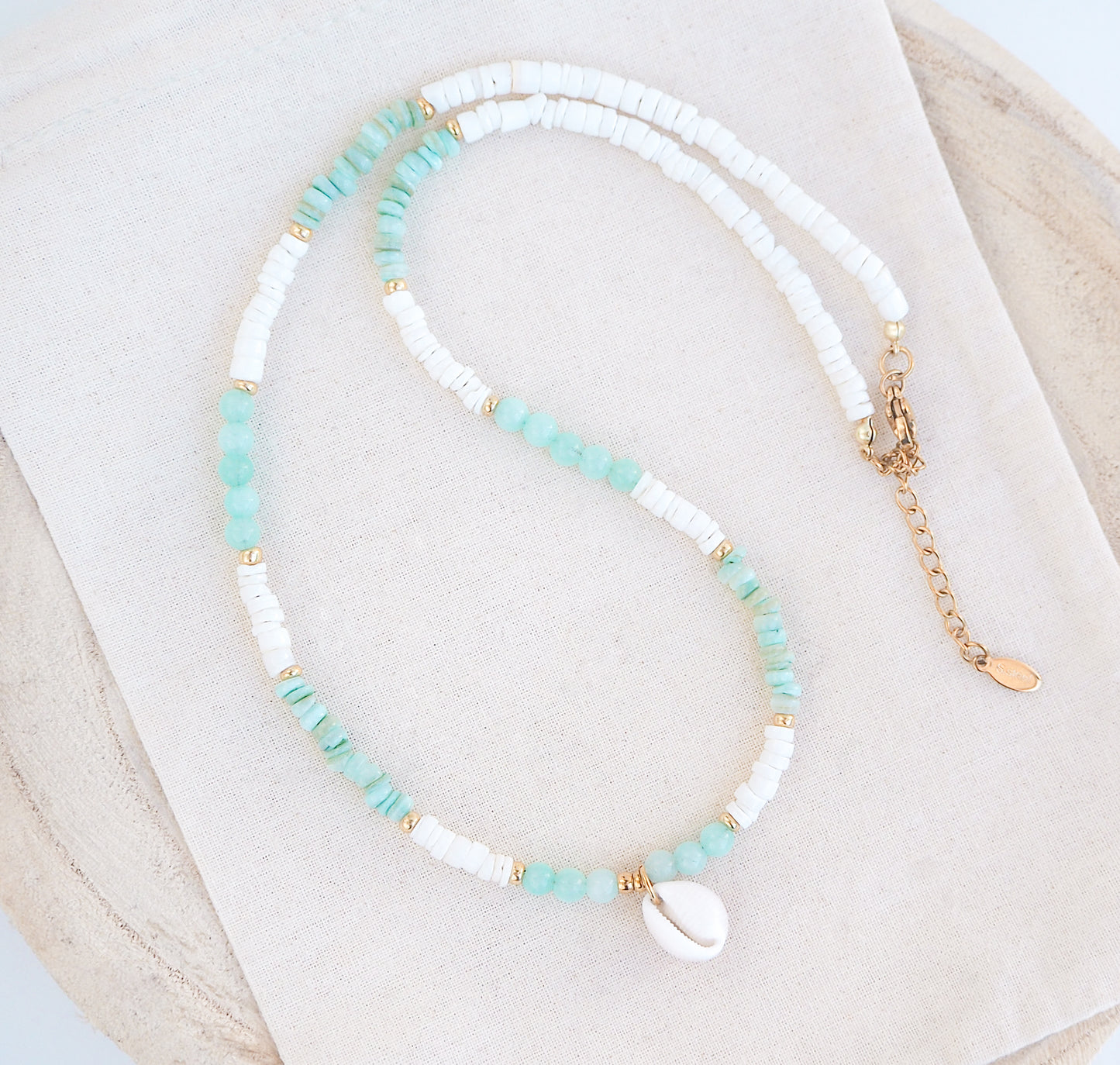 A cowrie necklace with soft green stone beads, jade beads and white shell beads. The center piece of this necklace is a Northern Cowrie Shell, handpicked from the beach of Portugal. The shell is white and about 1 cm.