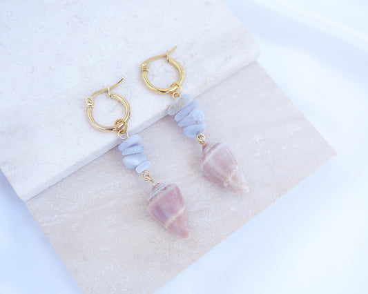 Gold Cone Shell Blue Gemstone Earrings displayed on light stone. Gold earring hoops with real Mediterranean Cone Shells from Portugal and blue agate gemstones. Made with 14k gold stainless steel hoop earrings.
