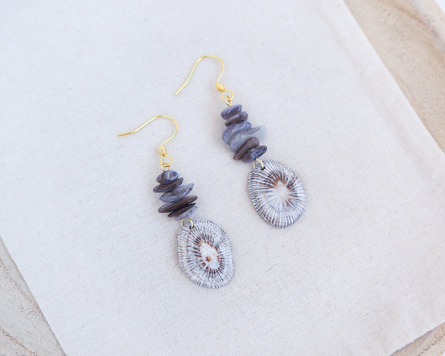 Gold hoop earring with shell and dark stones on cotton display. Gold Striped Limpet Shell Dark Grey Stone Drop Earrings. Gold hoops with real shells from Portugal. Made with 14k gold stainless steel hoop earrings.