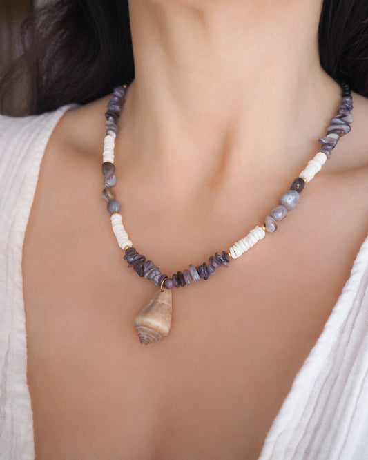 Model wearing a necklace with grey and white beads and a large cone shell pendant on a light background. A necklace with a mediterranean cone shell paired with Botswana agate gemstone beads and white shell beads. The shell is a mediterranean cone shell from Portugal and is about 3,5 cm. The color of the shell is brown.