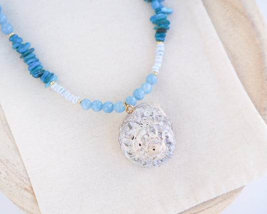 Close up of a necklace with a big star shell paired with aquamarine gemstone beads, turquoise stones and light blue shell beads on light background. The shell is a rough star shell from Portugal and is about 4 cm. The color of the shell is ivory grey.