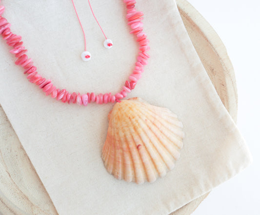 Close up of A scallop shell necklace with soft coral pink stone beads. The shell is a pilgrim's scallop shell from Portugal and has soft orange coral color.