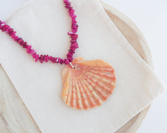 Close up of a big scallop shell necklace with fuchsia pink stones. Made with a real great scallop shell from Portugal. The shell has orange color with a coral pattern.
