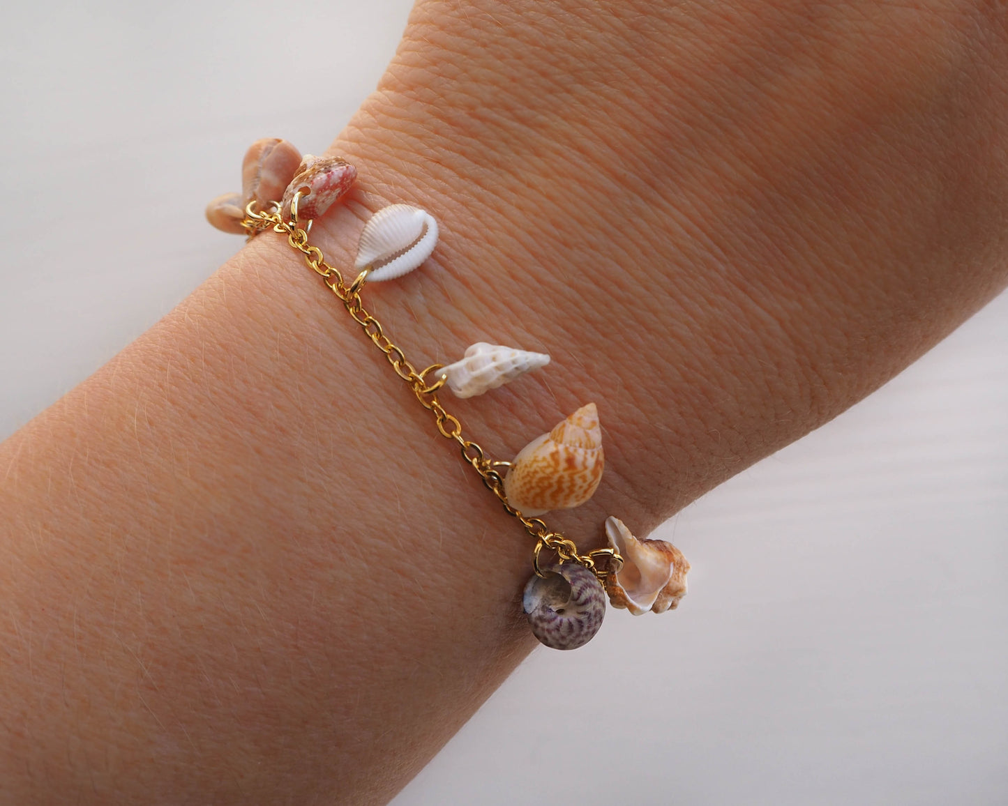 Model wearing Ocean Inspired Jewelry: 8 Tiny Shells on a Gold Stainless Steel Charm Bracelet - Mediterranean Cone, European Cowrie, Flat Topshell, Rustic Dove, Common Wentletrap, Sting Winkle, European Painted Topshell, Nassa Mud Shell