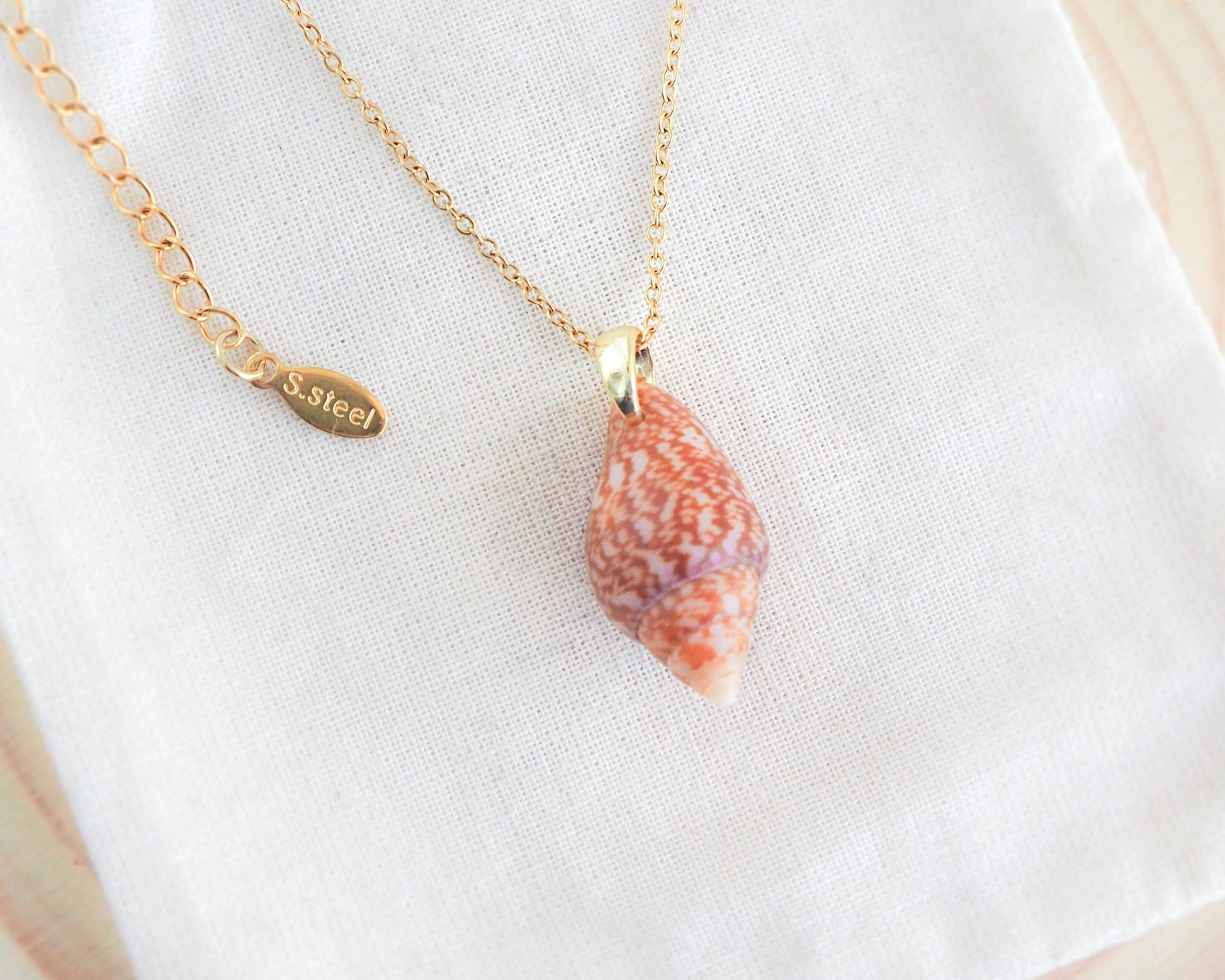 Close-up of the lustrous gold stainless steel chain adored with a Rustic dove shell from Portugal, gleaming in radiant light, adding a touch of sophistication to the necklace. Beach Girl gift, sea by lou