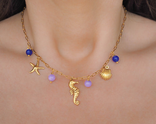 Model wearing charm necklace with gold seahorse, starfish and shell