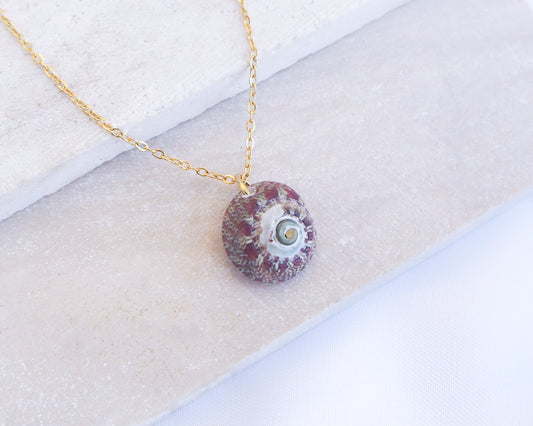 Necklace with a red and white stone pendant on a textured surface. Bordeaux Green Patterned Flat Top Shell Gold Necklace on display close up