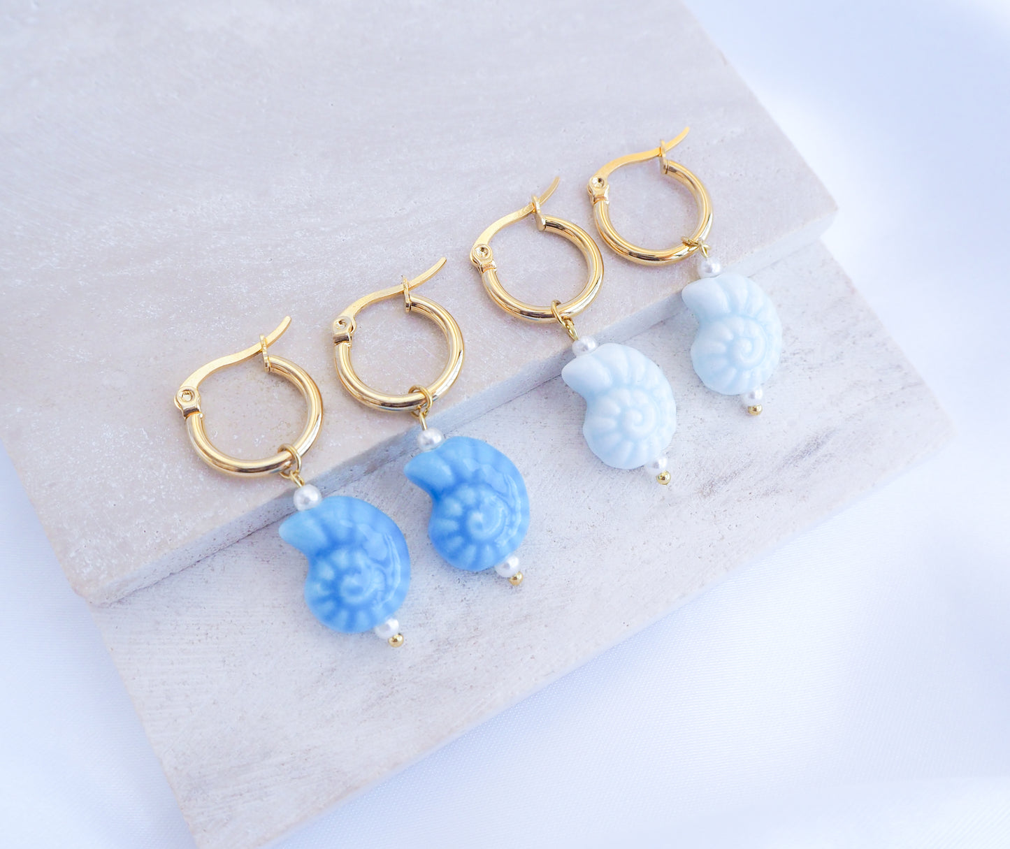 Gold hoop earrings with blue seashell-like charms on a light gray surface.