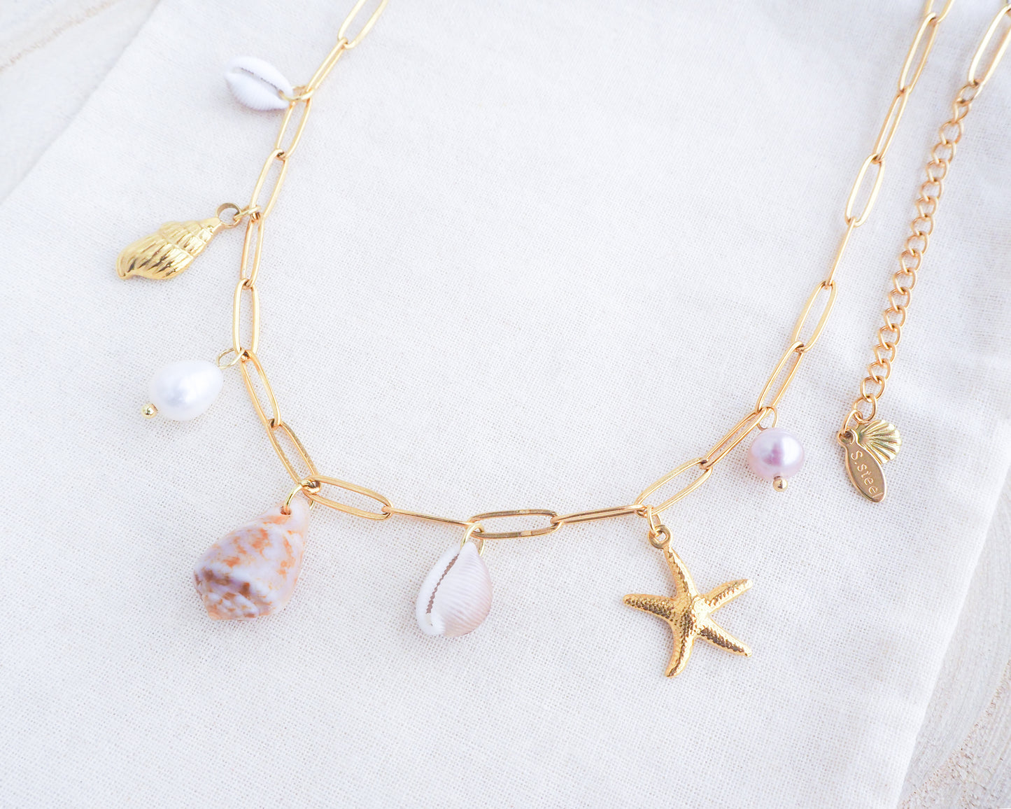 Gold Ocean Shell Charm Necklace on display side view, tiny cone and cowrie shells, freshwater pearls, starfish sea star and whale tail pendants.