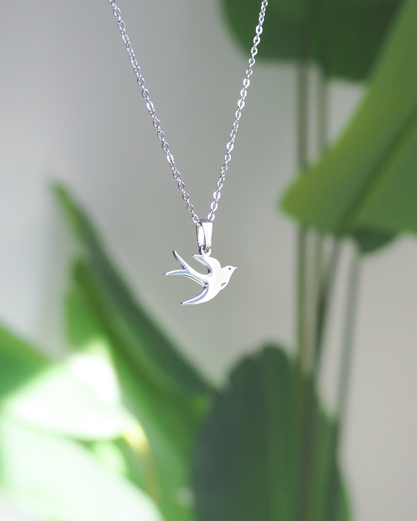 Silver Swallow Bird Necklace front view with plant background, made of stainless steel