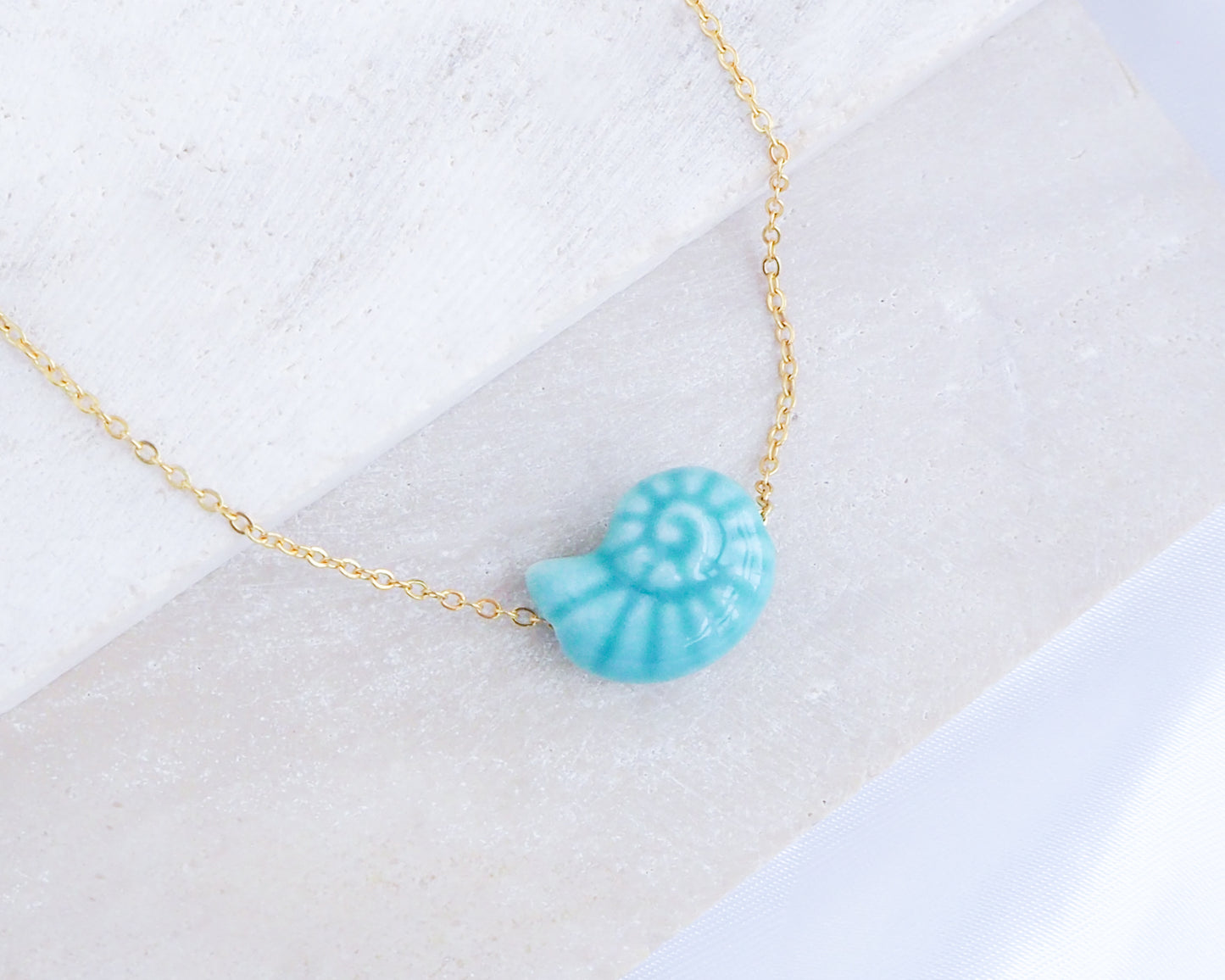 Turquoise Blue Ceramic Seashell Nautilus Gold Necklace on stone display