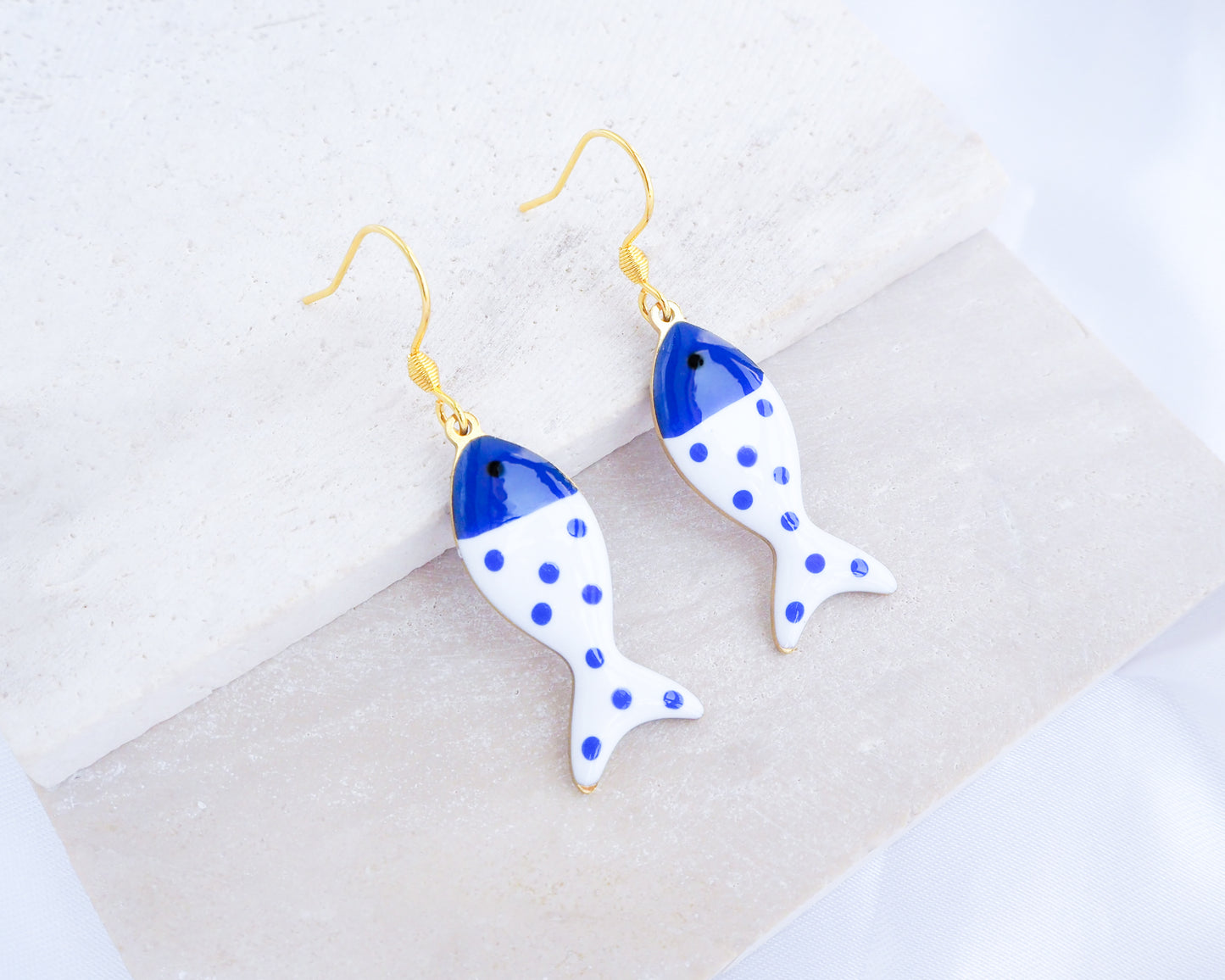 White Blue Polka Dot Sardine Fish Earrings displayed on stone, 14k gold stainless steel earring hooks, summer drop earrings from Portugal